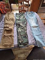 Front view of all three pairs laid flat: tan cargo, camo cargo, light blue jeans