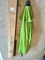 Folded lime green patio umbrella with black finial, separate lower pole section, original box visible