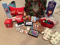 Group shot of entire lot including wreath, pillow, Peanuts tree box, tub with ornaments, oven mitts, towels, tin and assorted decor