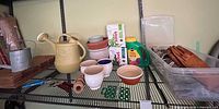Shelved gardening items including watering cans, pots, fertilizer, twine, plant ties