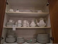 Cabinet view showing stacked plates, bowls, cups, pitchers