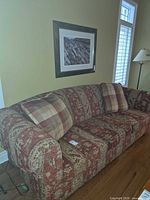 Full view of patterned three-seat sofa against wall with two plaid cushions