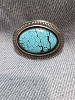 Front view of sterling silver belt buckle showing turquoise cabochon with spiderweb matrix and scalloped border