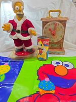 Group shot: Santa Homer figure, Fisher-Price clock, Mickey Mouse tin, Elmo bag