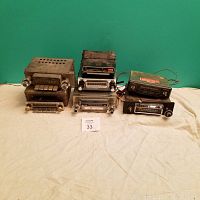Photo of 7 vintage car audio devices arranged in two rows on fabric background with green wall