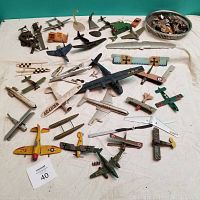 Wide view of broken model airplanes laid out on white cloth showing multiple incomplete and damaged wooden and plastic models with various paint styles.
