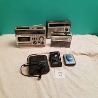 Front view of five vintage radios and cassette players on a cloth surface against teal background.