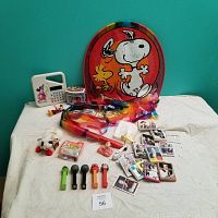 Full view showing damaged Snoopy kite, Mickey Math calculator, Pez dispensers, Lamb Chop toy, Planes toy, and multiple trading cards spread out on a white sheet.