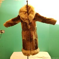 Full front view of the rabbit fur coat with large fox fur collar and bottom trim, coat hung on a hook against a plain wall.