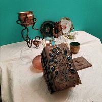 Photo showing mixed decor items on a white cloth against teal wall including secret book box, plates, wood carving, fishbowl, plant stand