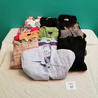Full view of folded clothing items including sweaters, blazer, and tops stacked on a surface showing variety of styles and colors.