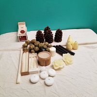 Wide view showing all candle types and the gold pine cone ornaments on white cloth background