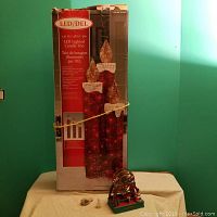 Photo showing the original boxed LED lighted candle trio next to the battery operated Christmas Ferris wheel and some small decorative pieces on a beige cloth against a green wall.