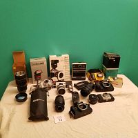 Wide view of all items showing Kodak EK6 camera, assorted lenses, flashes, yellow Kodak camera, novelty lens-shaped travel mug