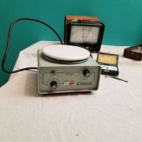 All items arranged on beige cloth: TherMixyne Heat/Stir Plate front view with knobs, Simpson meter, sphygmomanometer case, and weight set visible.