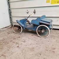 Side view of the blue wooden toy car showing metal steering wheel, rubber tires on metal spoked wheels, and overall wear on paint.