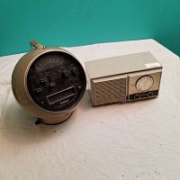 Photo showing two radios side by side on a white surface against turquoise background. One radio is round with melted brown case and black front panel (Zenith). The other is rectangular beige with front speaker grill and tuning dial (Fleetwood).