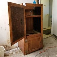 Front view of the wooden ice box with the upper door open showing interior shelves and compartments.