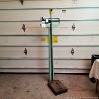 Full frontal view of the vintage green Health-o-meter scale showing base, vertical height rod, and mechanical balance beam scale section.