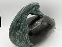 Side view of carved stone duck showing green patina on neck and head, black stone body