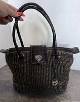 Front view showing woven straw body, leather trim, heart logo plate and charm