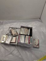 Overall view of box containing numerous cassette tapes with some loose tapes beside it