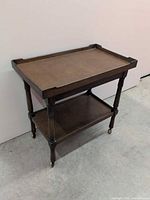 Full view of wooden rolling cart, two tiers, leather top, brass casters