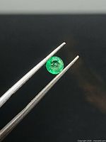 Emerald held in tweezers, showing size and color