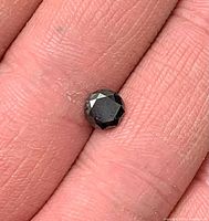 Loose black diamond on fingertip showing table and facets