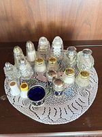 Group view of all shakers and condiment pot on lace doily
