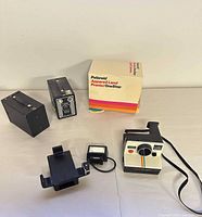 Group shot of Polaroid camera, Kodak Brownie camera front and rear views, Nissin flash with bracket and Polaroid box