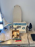 Overall lot showing sewing machine, buttonholer, manual, lamp, iron, ironing board