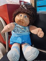 Full view of doll seated, showing clothing and overall condition