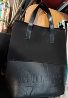 Front of black Guess tote showing embossed logo and handles