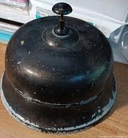 Top and side view of black metal bell showing overall form and paint wear