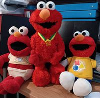 Front view of all three Elmo plush toys seated on table