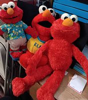 Three Elmo plush toys grouped together on desk