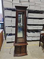 front view of tall wood display cabinet with glass door, mirrored back, interior shelves and lower cabinet