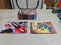 Stack of 10 Injustice trade paperbacks with two separate Supergirl books displayed
