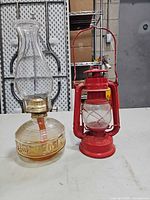 Both items together: glass oil lamp on left, red railroad lantern on right