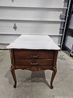 Front view showing drawer, brass hardware, ornate legs, marble top