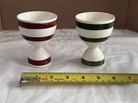 Front view of both striped cups alongside tape measure for scale
