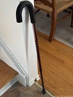 Full view of copper-tone Airgo adjustable cane leaning against wall