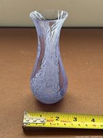 Side view of lavender and white swirled glass bud vase with tape measure showing height