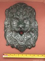 Front view of painted plaster lion head plaque with ruler for scale
