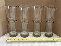 Four clear glass beer glasses lined up with measuring tape showing height