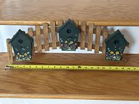 Full view of fence panel with three birdhouse fronts and measuring tape indicating width