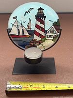 Front view of round stained glass lighthouse tea light holder on stand with tape for scale