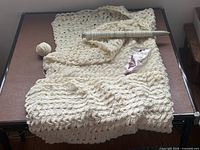 Overview of knitted throw draped on table with needle and yarn