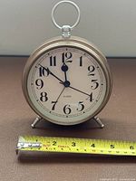 Front view of round brass-tone alarm clock with tape measure showing width
